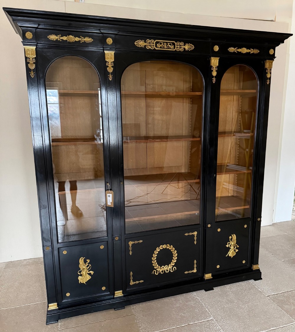A large ebonised three-door glazed bookcase featuring gold-toned gilt-bronze mounts, arched glass panels, and an oak interior. View XVI