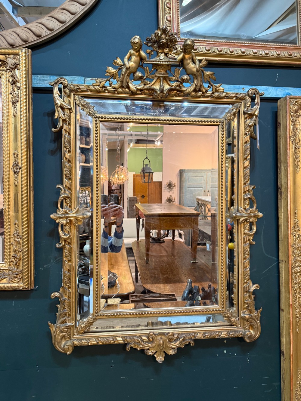 A 19th-century rectangular French giltwood wall mirror featuring elaborate cresting with cherubs, an urn finial, acanthus leaf scrolling, and a beaded inner border around a bevelled glass plate.