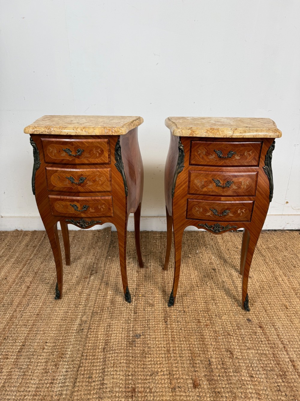 A pair of French Louis XV style bedside cabinets featuring variegated yellow marble tops, three marquetry inlaid drawers, brass mounts, and slender cabriole legs. View II