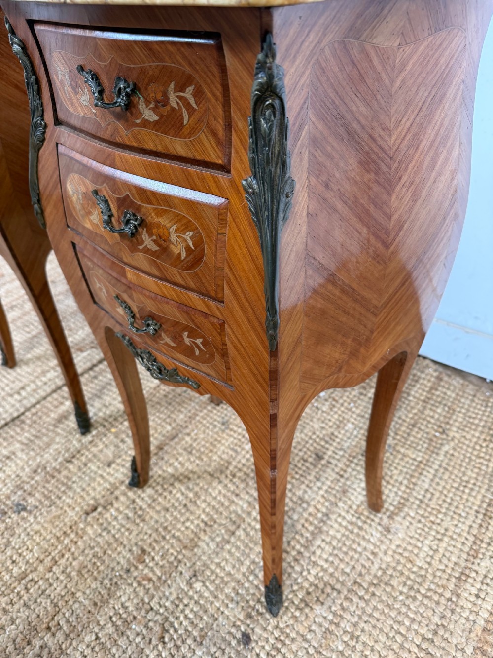 A pair of French Louis XV style bedside cabinets featuring variegated yellow marble tops, three marquetry inlaid drawers, brass mounts, and slender cabriole legs. View IV