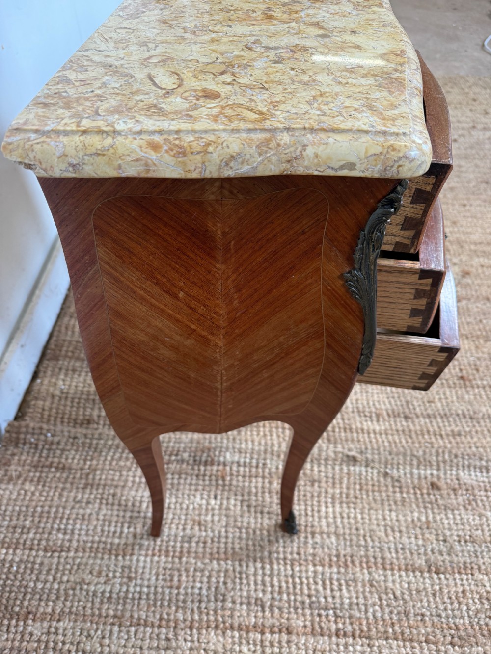 A pair of French Louis XV style bedside cabinets featuring variegated yellow marble tops, three marquetry inlaid drawers, brass mounts, and slender cabriole legs. View VI