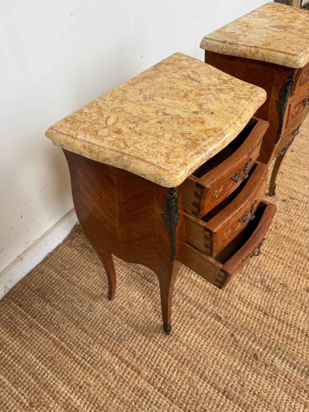 A pair of French Louis XV style bedside cabinets featuring variegated yellow marble tops, three marquetry inlaid drawers, brass mounts, and slender cabriole legs. View VIII
