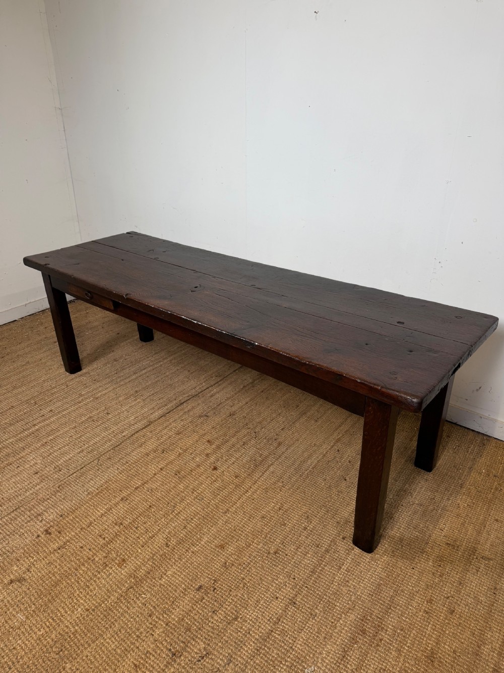 A long 18th century dark oak farmhouse dining table with a thick plank top and square legs.