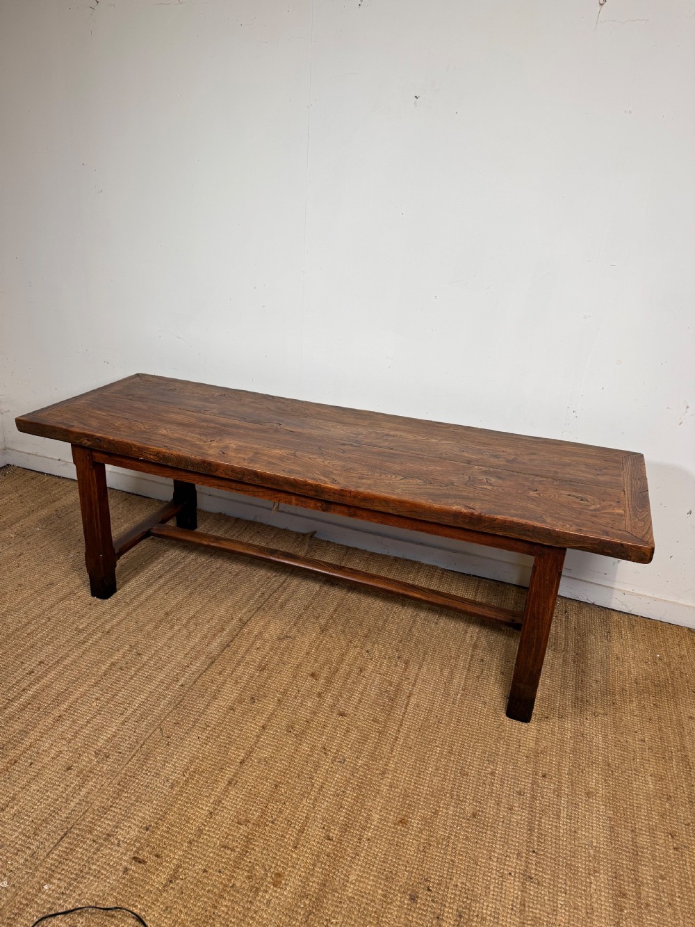 A long 19th-century rustic elm farmhouse dining table featuring a solid plank top and lower support stretchers.