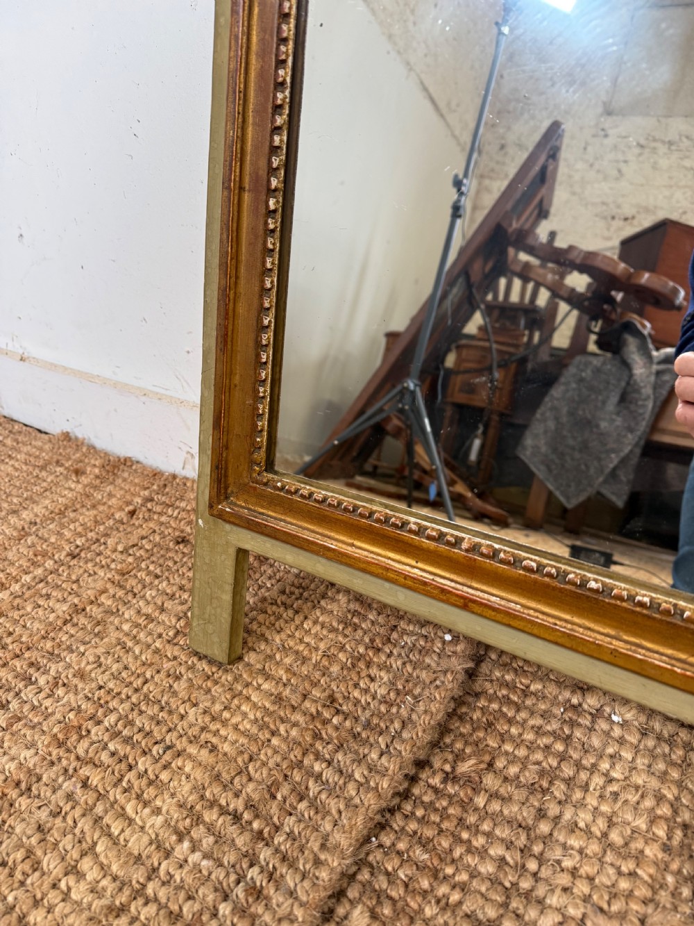 A compact Louis XVI style wall mirror featuring a gilded carved wood frame with beaded moulding and a prominent floral crest. View IV