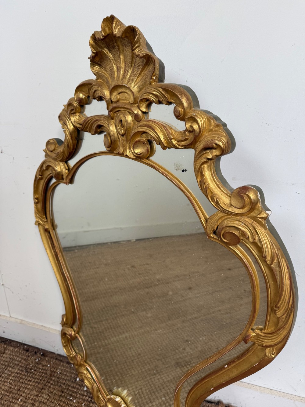 A French style carved giltwood wall mirror featuring an ornate shell crest and C-scroll border around an asymmetrical glass pane. View II