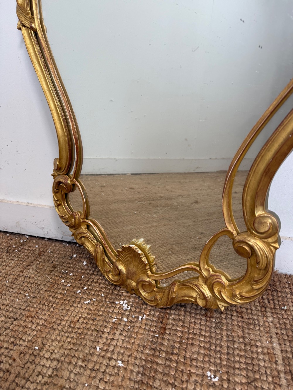 A French style carved giltwood wall mirror featuring an ornate shell crest and C-scroll border around an asymmetrical glass pane. View III