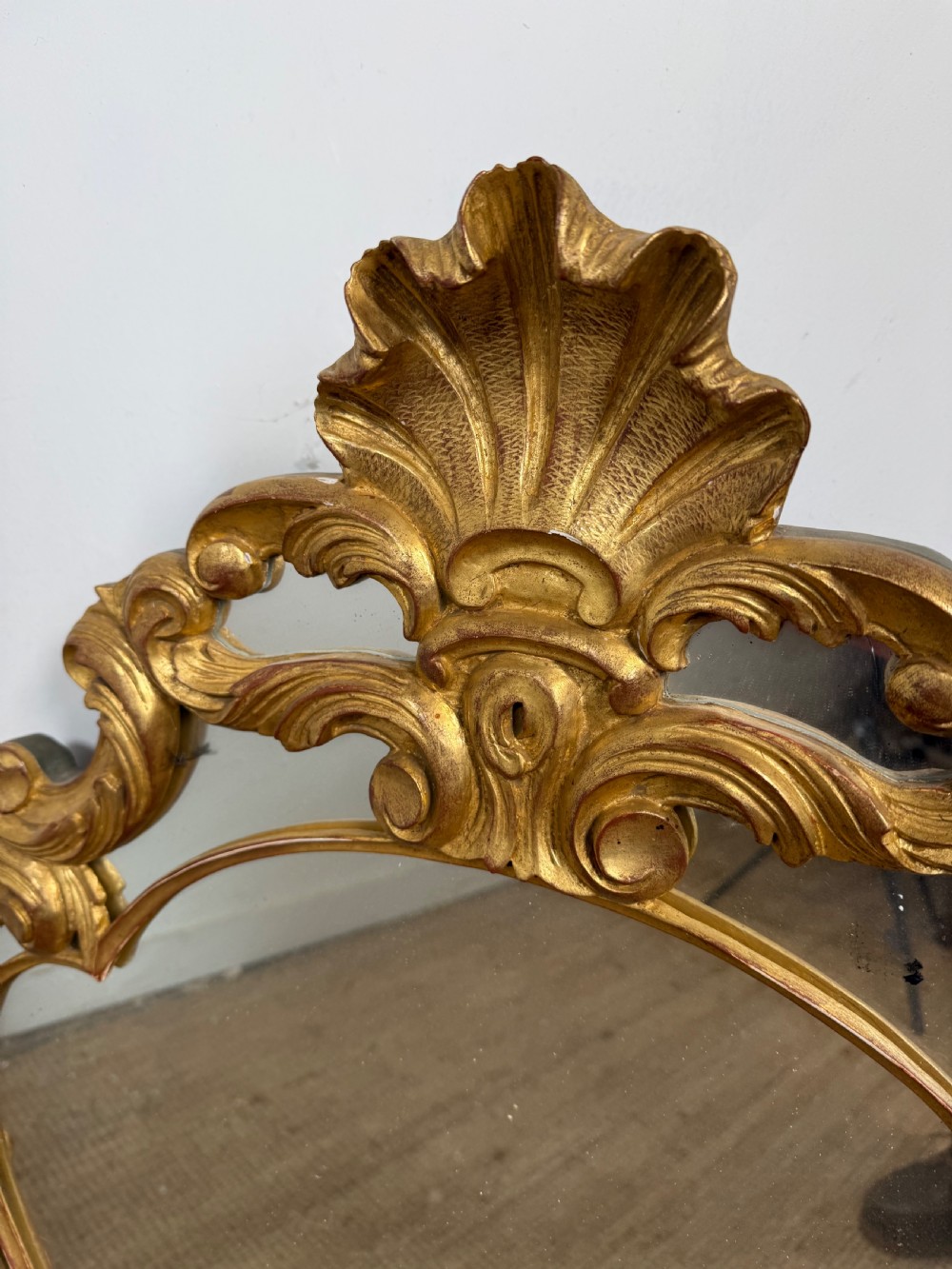 A French style carved giltwood wall mirror featuring an ornate shell crest and C-scroll border around an asymmetrical glass pane. View IV