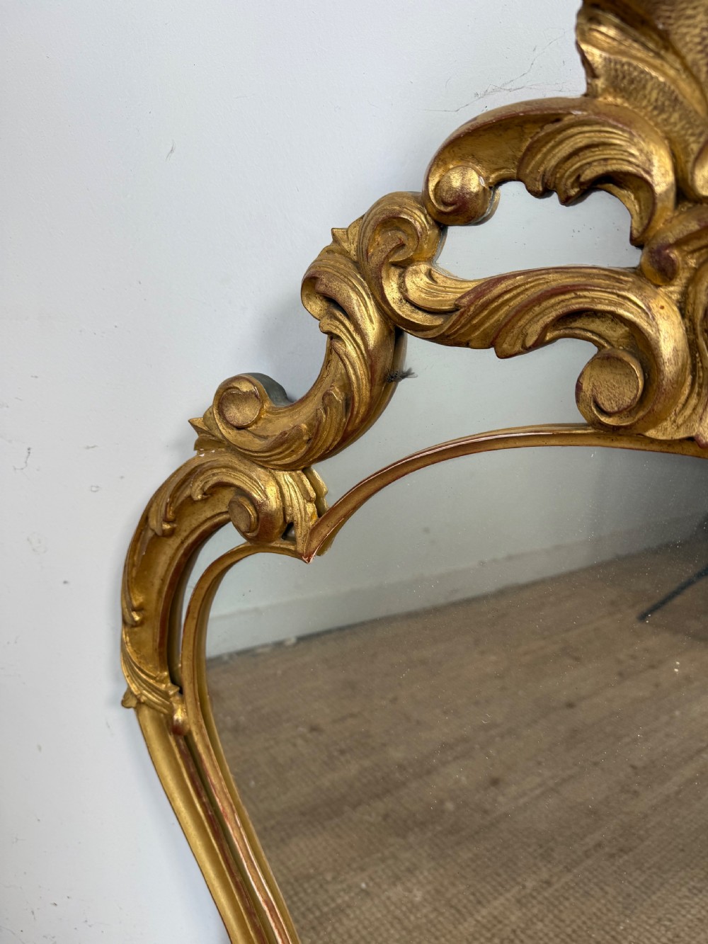 A French style carved giltwood wall mirror featuring an ornate shell crest and C-scroll border around an asymmetrical glass pane. View V