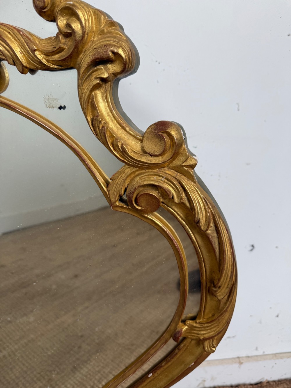 A French style carved giltwood wall mirror featuring an ornate shell crest and C-scroll border around an asymmetrical glass pane. View VI