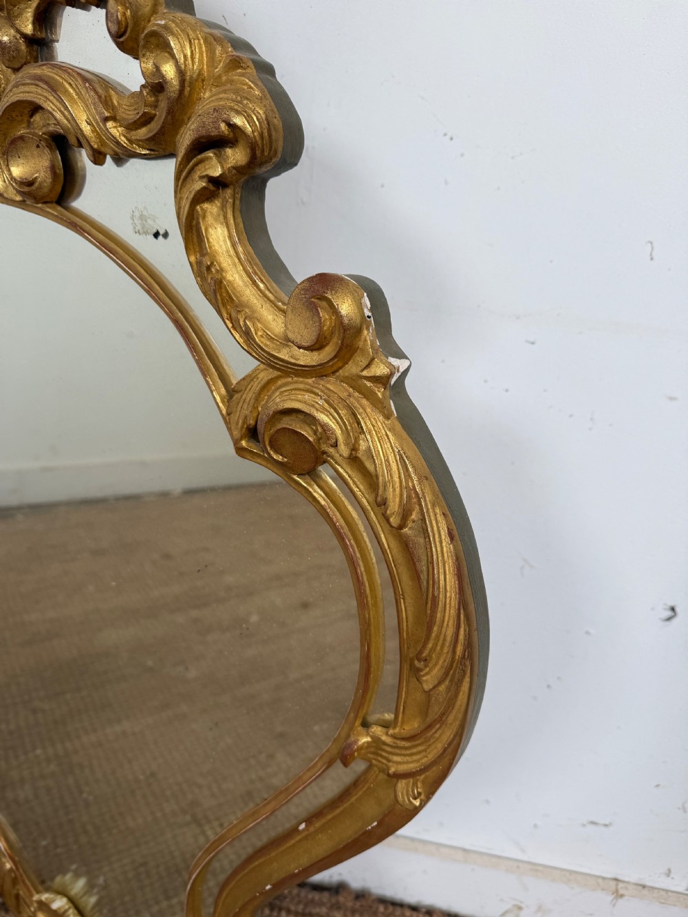 A French style carved giltwood wall mirror featuring an ornate shell crest and C-scroll border around an asymmetrical glass pane. View VII