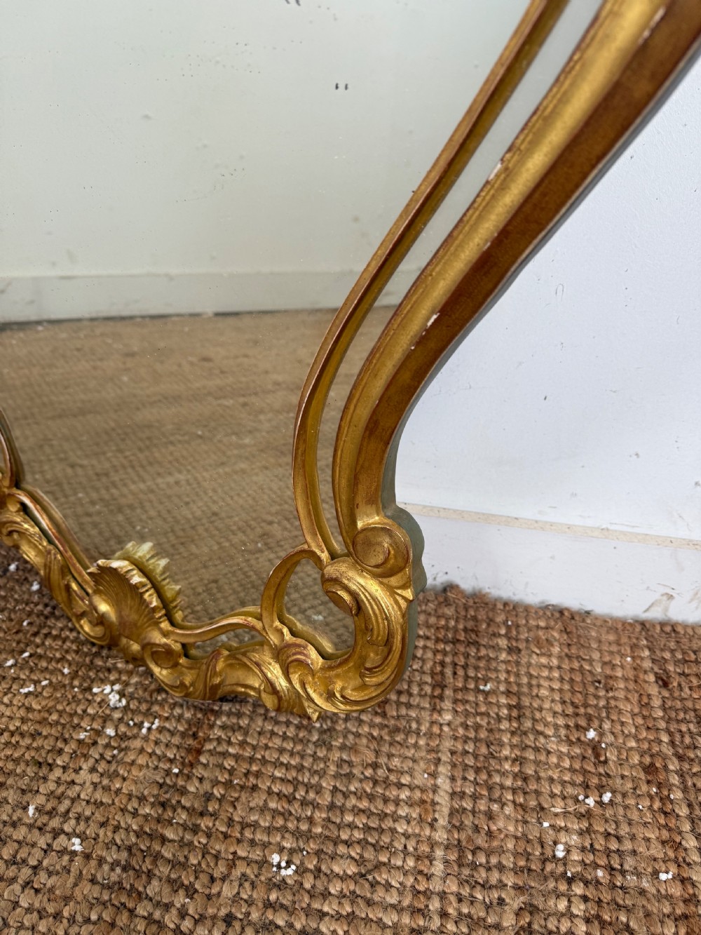 A French style carved giltwood wall mirror featuring an ornate shell crest and C-scroll border around an asymmetrical glass pane. View VIII
