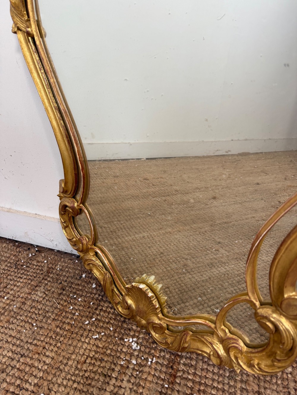 A French style carved giltwood wall mirror featuring an ornate shell crest and C-scroll border around an asymmetrical glass pane. View IX