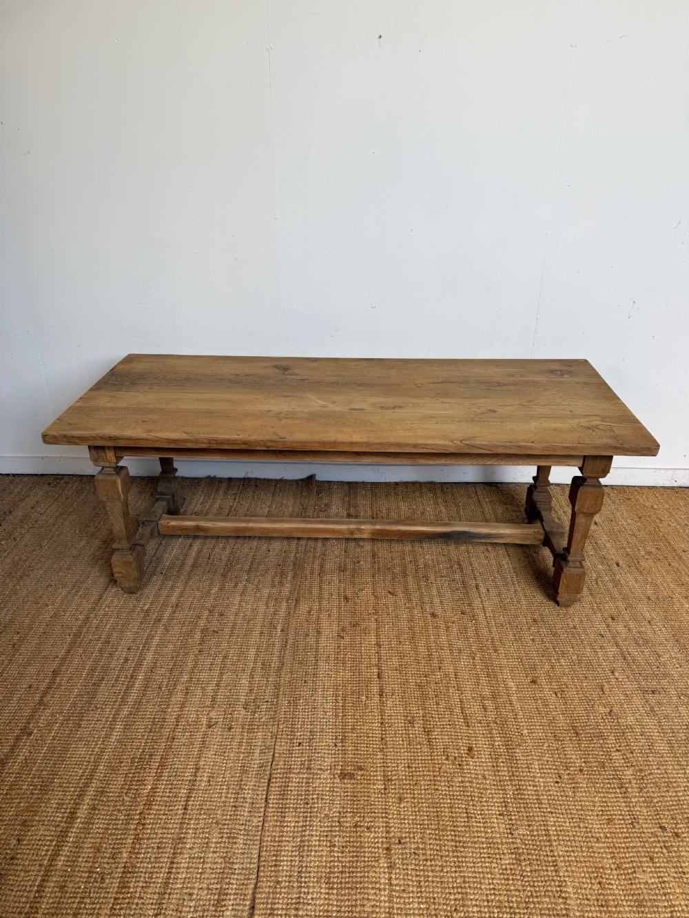 A long rectangular scrubbed oak refectory table featuring a solid top and trestle base with a low central stretcher.