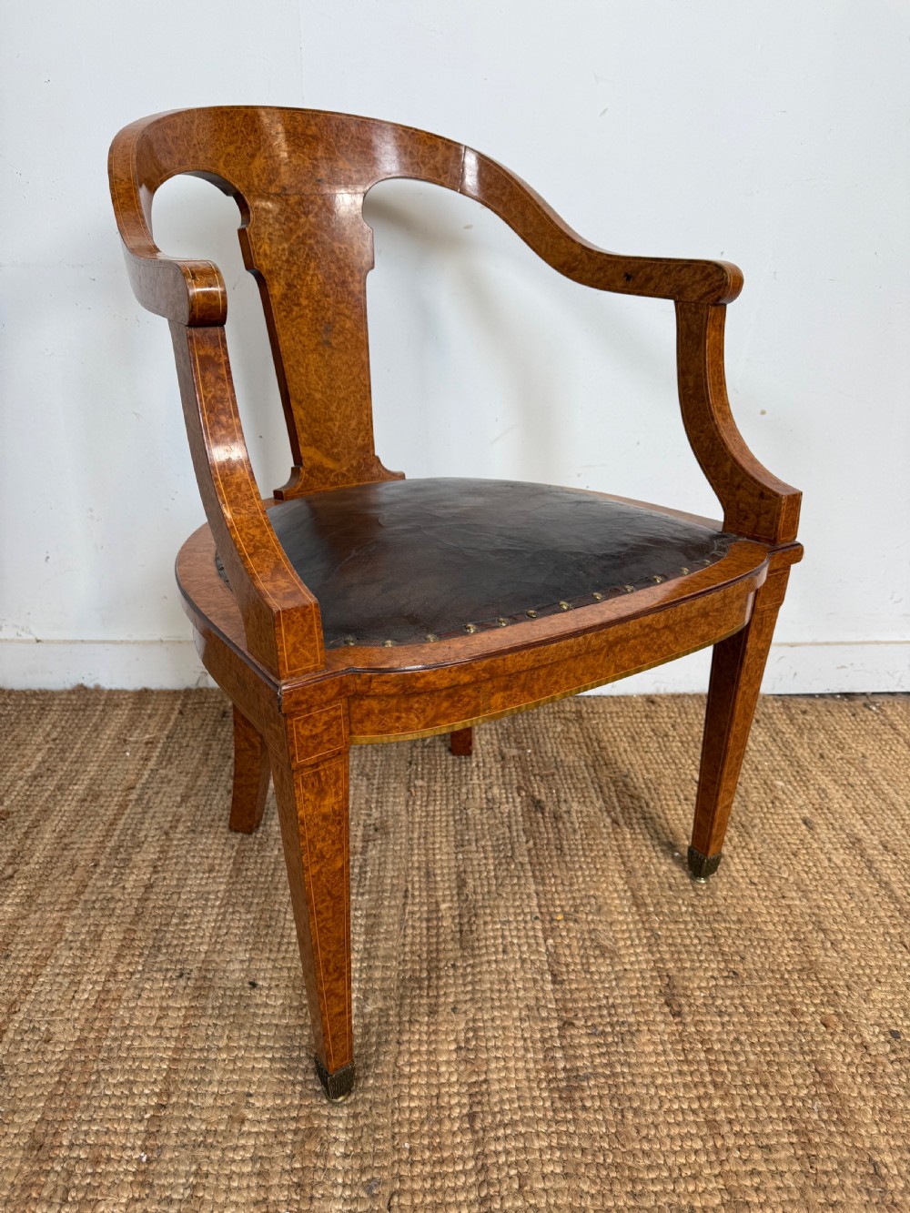 Late 19th-century burr elm desk chair featuring a curved backrest, central splat, dark leather studded upholstery, and tapered legs with brass feet.
