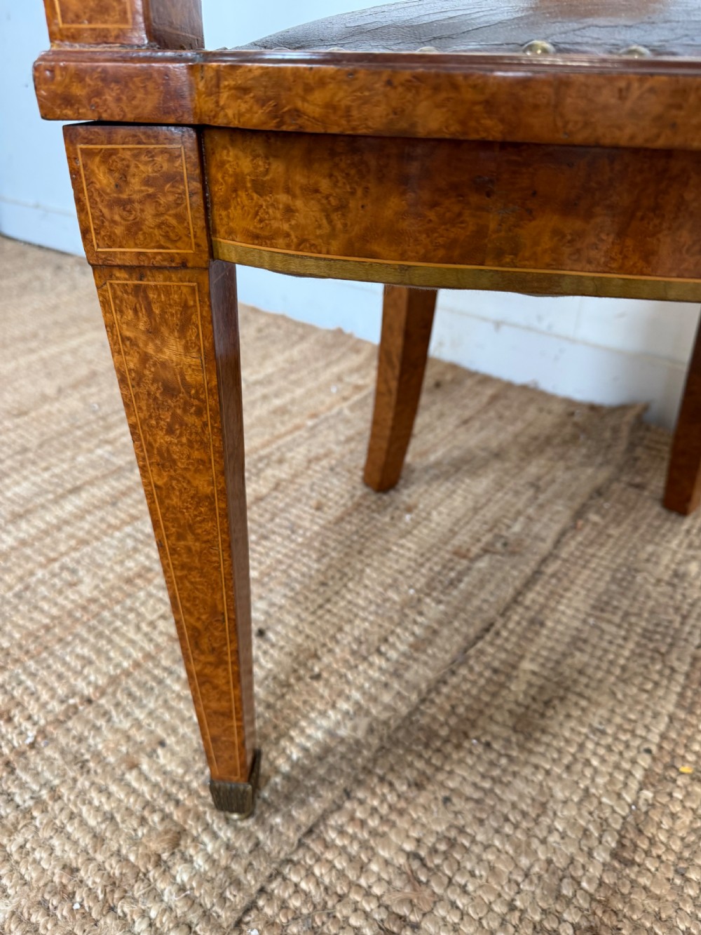 Late 19th-century burr elm desk chair featuring a curved backrest, central splat, dark leather studded upholstery, and tapered legs with brass feet. View X