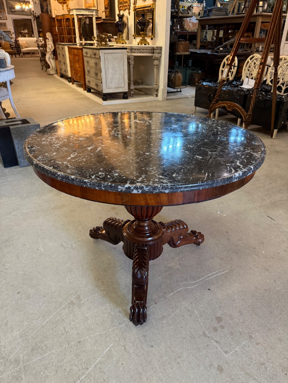 A 19th-century circular centre table featuring a dark veined marble top supported by a carved mahogany pedestal stem and a tripartite claw-foot base.
