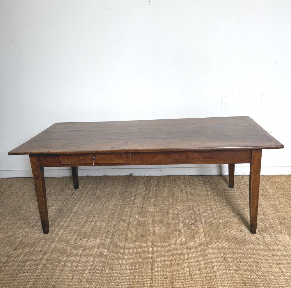 An antique French cherrywood farmhouse dining table featuring a plank top, single frieze drawer, and four square tapered legs.