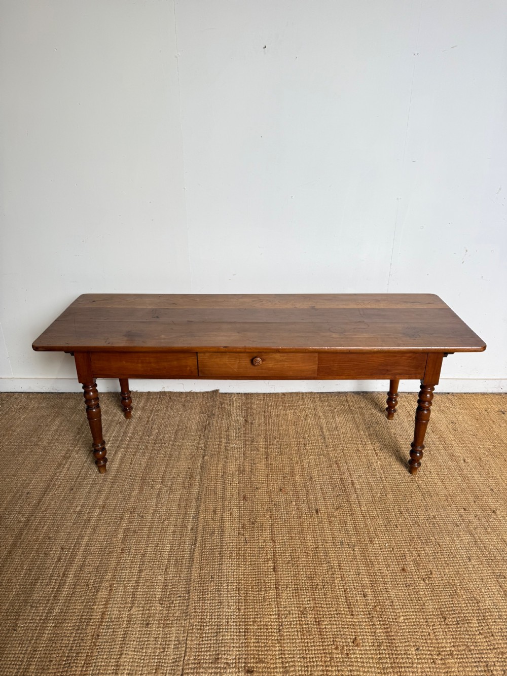 An antique rectangular cherrywood console table with a plank top, single central drawer with a turned knob, and four baluster turned legs.