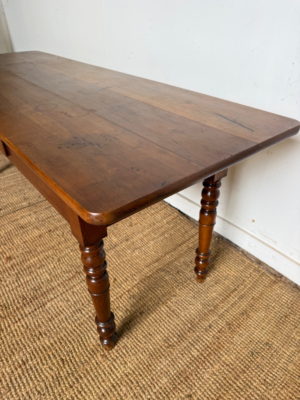 An antique rectangular cherrywood console table with a plank top, single central drawer with a turned knob, and four baluster turned legs. View III