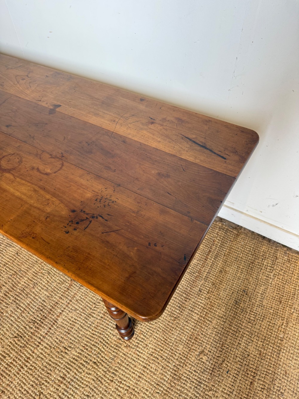 An antique rectangular cherrywood console table with a plank top, single central drawer with a turned knob, and four baluster turned legs. View IV
