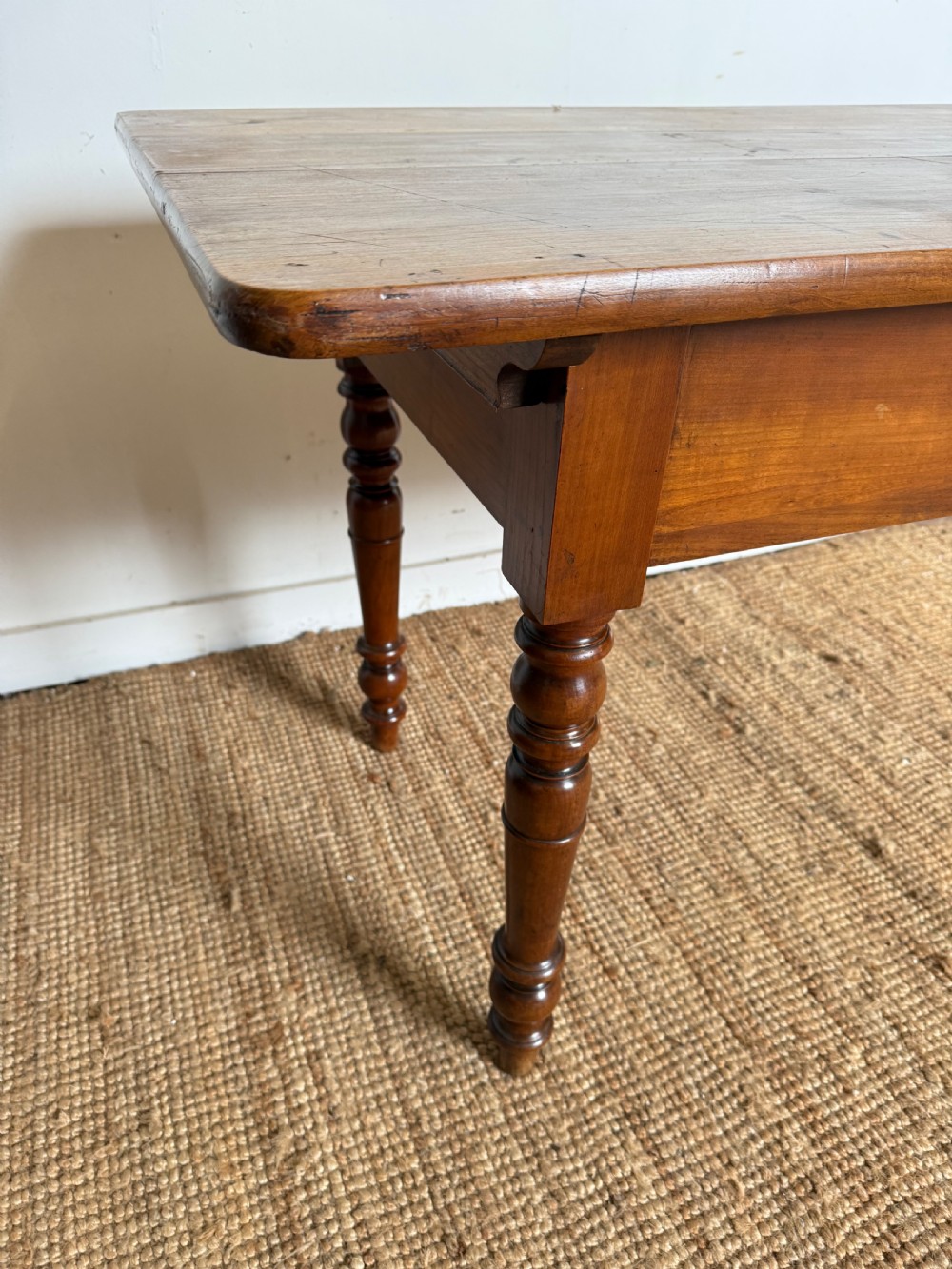 An antique rectangular cherrywood console table with a plank top, single central drawer with a turned knob, and four baluster turned legs. View V