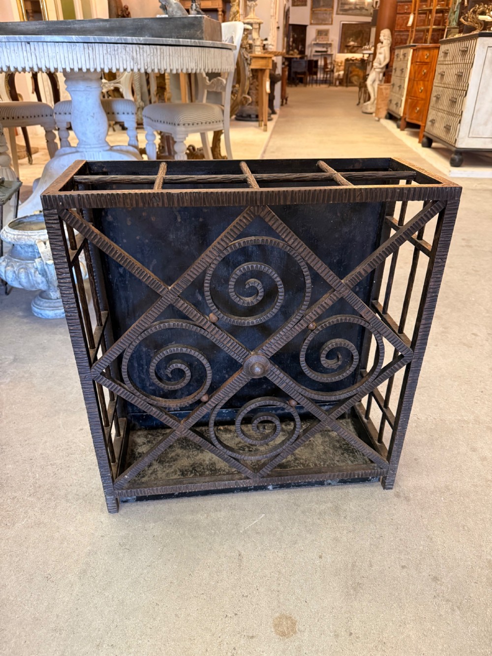 An Art Deco wrought iron umbrella stand featuring a dark hammered finish, central spiral motifs inside a diamond frame, and top section dividers.