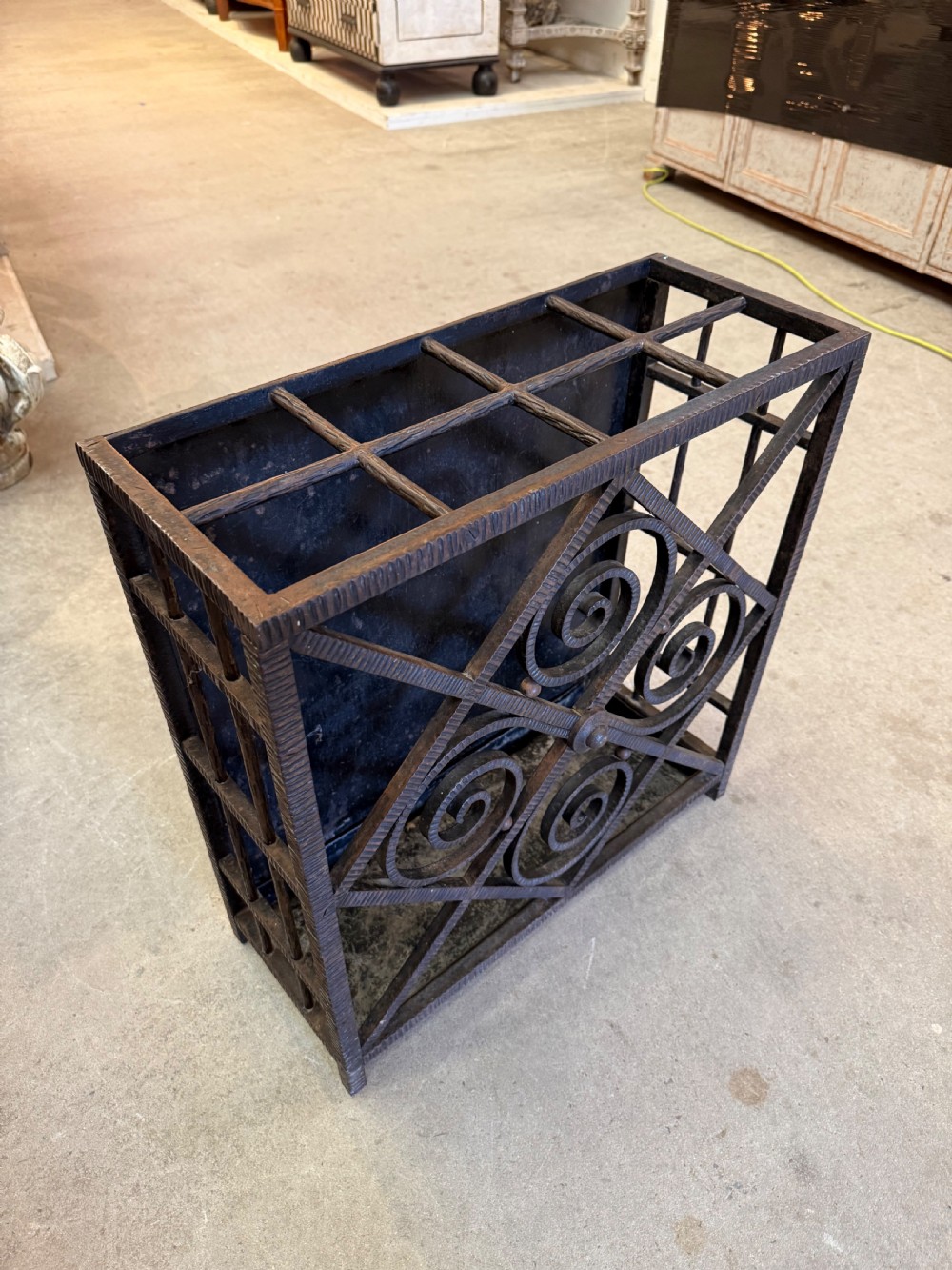 An Art Deco wrought iron umbrella stand featuring a dark hammered finish, central spiral motifs inside a diamond frame, and top section dividers. View II