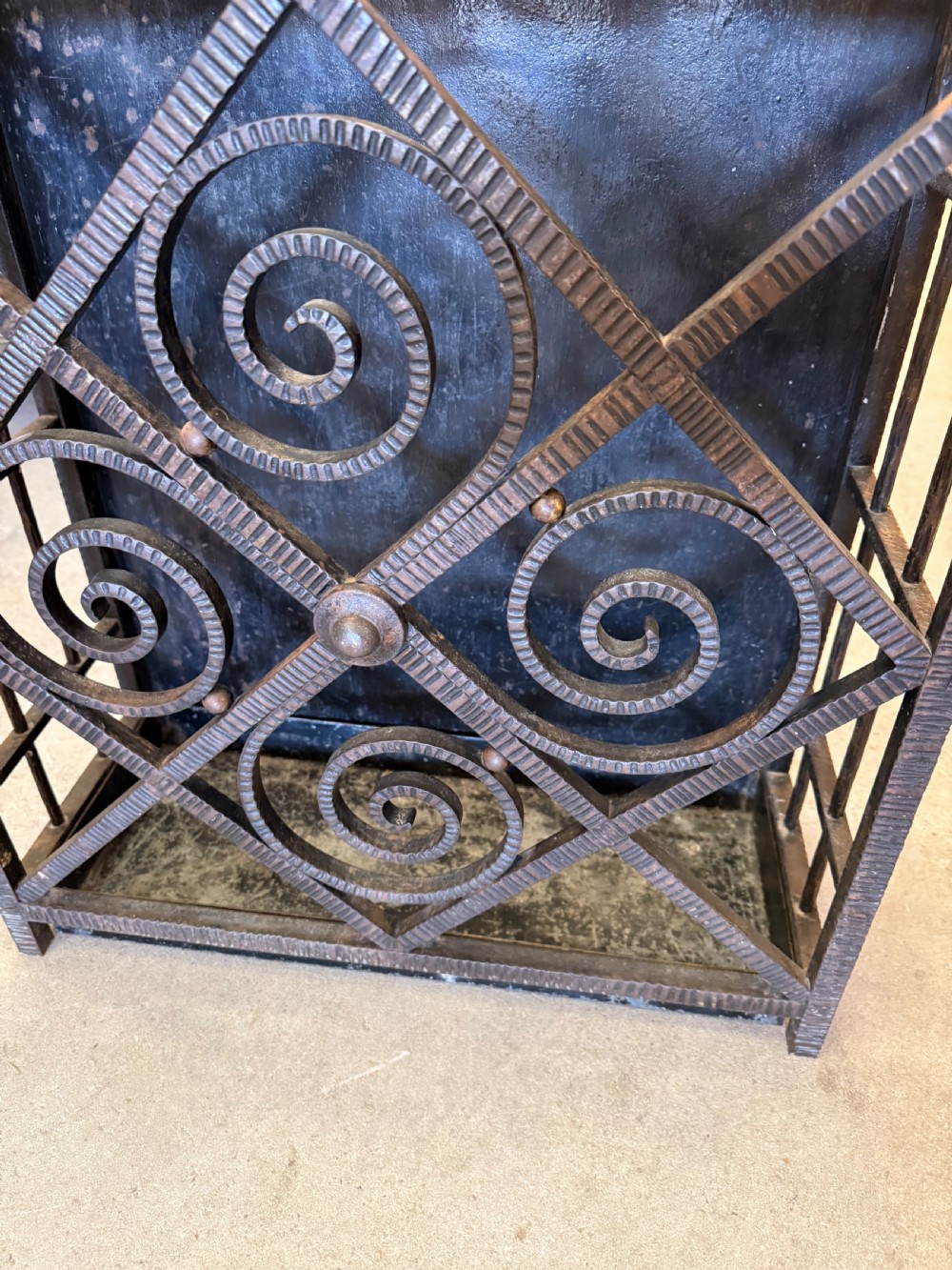 An Art Deco wrought iron umbrella stand featuring a dark hammered finish, central spiral motifs inside a diamond frame, and top section dividers. View V