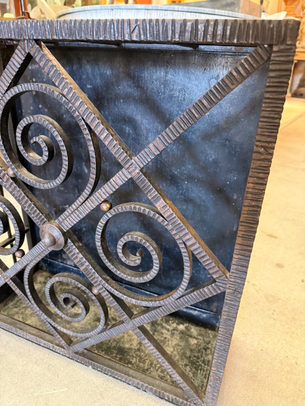 An Art Deco wrought iron umbrella stand featuring a dark hammered finish, central spiral motifs inside a diamond frame, and top section dividers. View VI