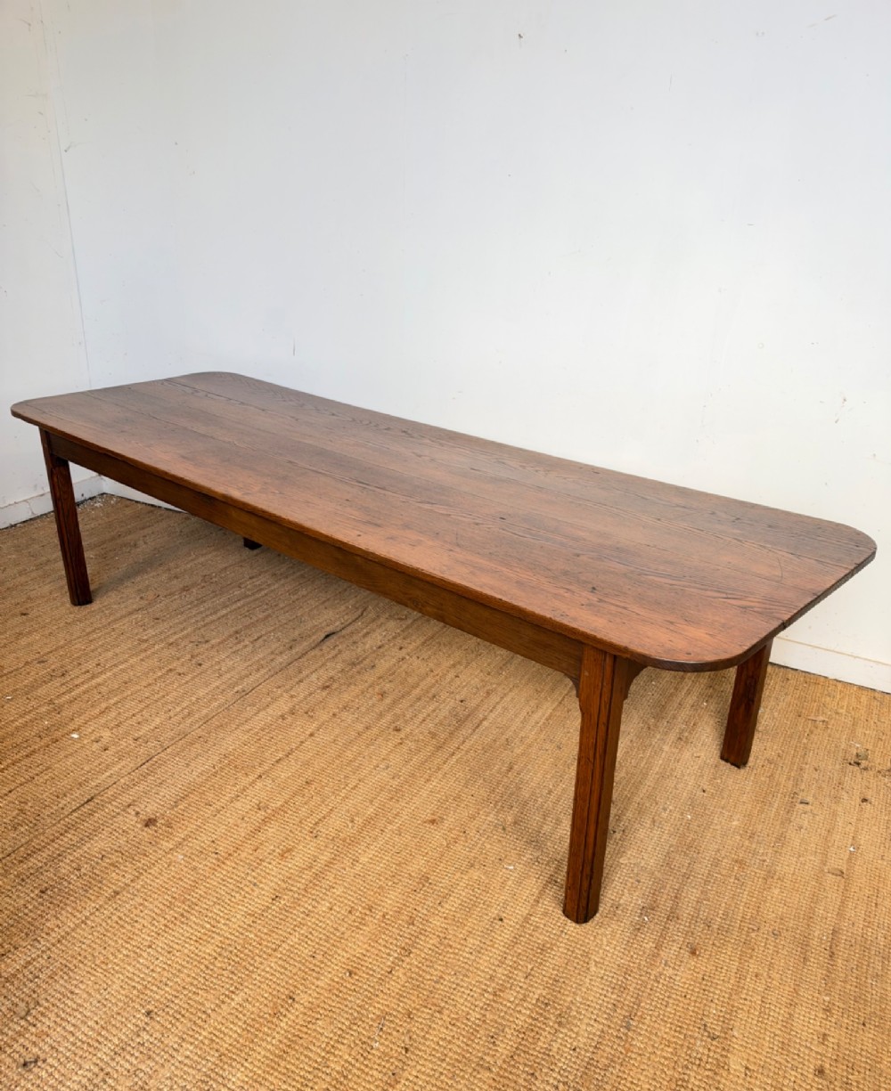 A large late nineteenth-century solid oak farmhouse dining table featuring a plank top with rounded corners and four straight legs.
