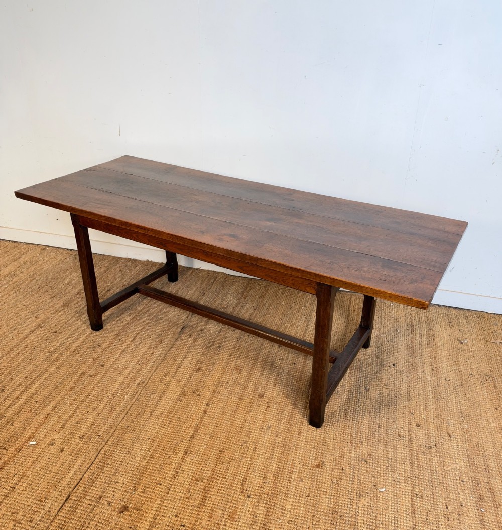 A rustic rectangular cherrywood farmhouse dining table with a three-plank top and an H-stretcher base.