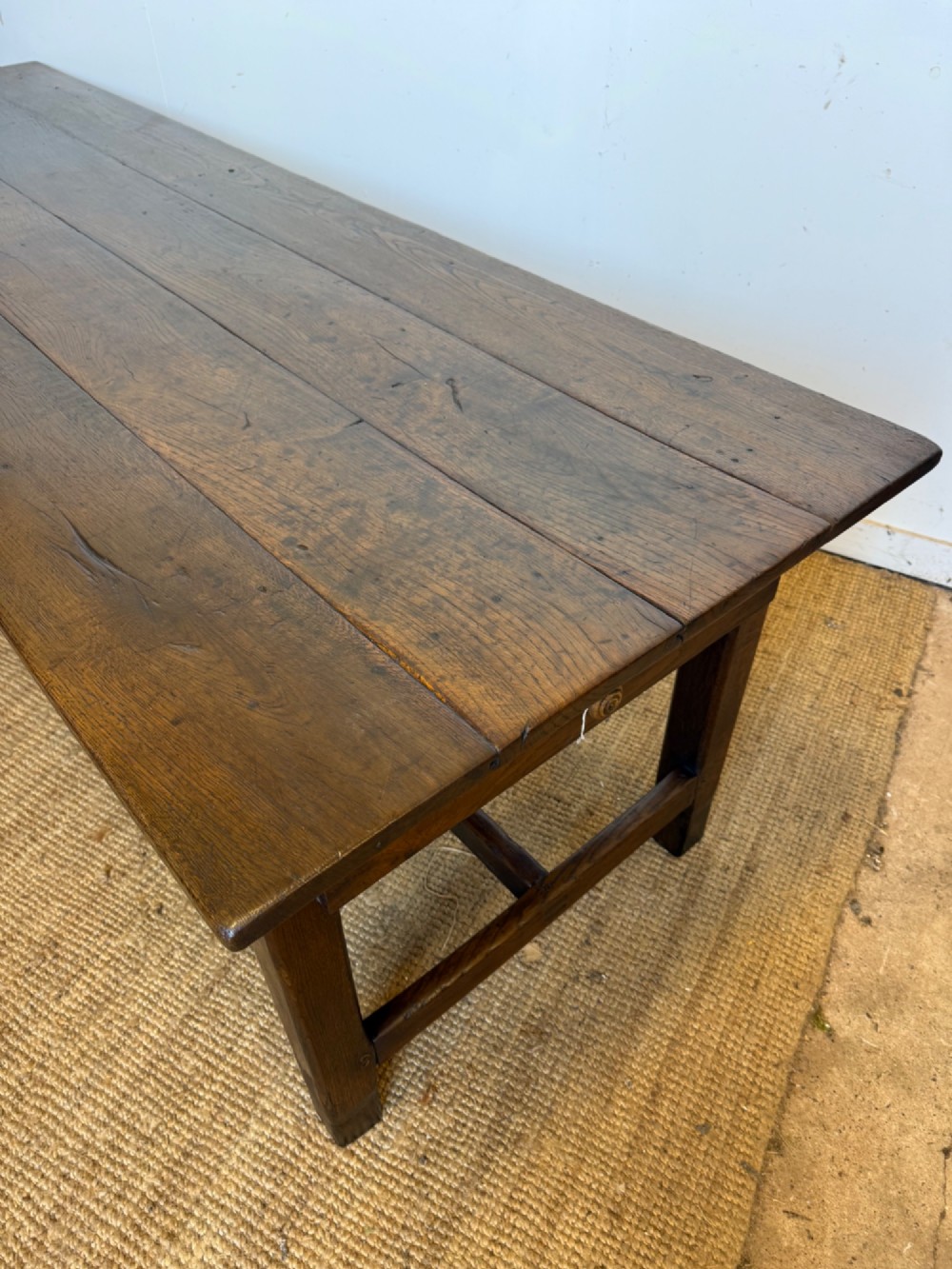 A long dark oak French farmhouse dining table with a plank top and an H-stretcher base structure. View II