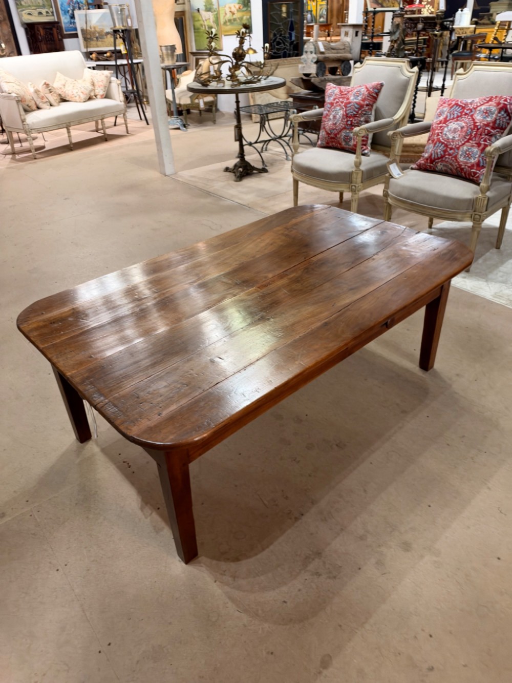 A low rectangular cherrywood coffee table featuring a plank top with rounded corners, tapered square legs, and a small side drawer.