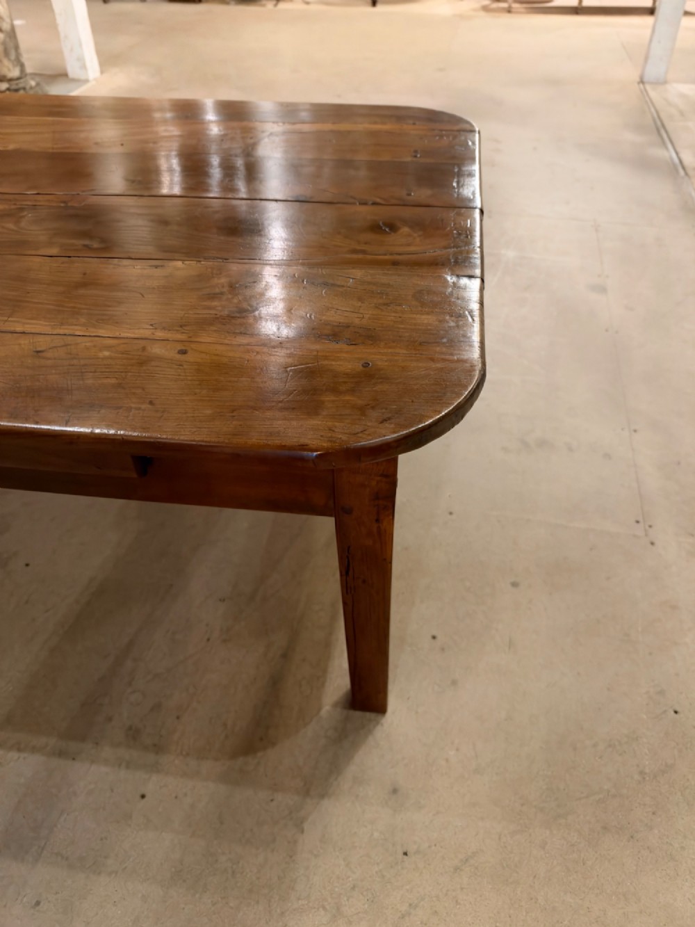 A low rectangular cherrywood coffee table featuring a plank top with rounded corners, tapered square legs, and a small side drawer. View V
