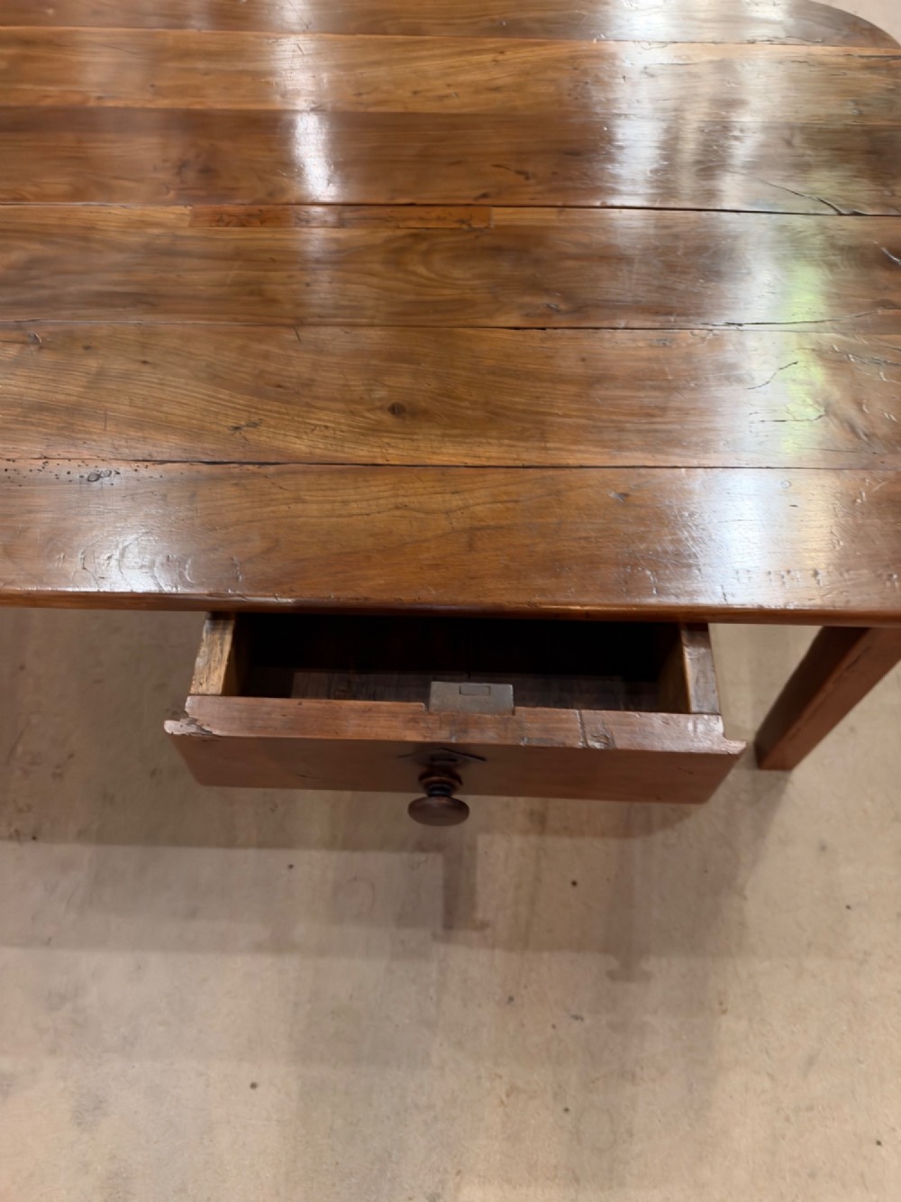 A low rectangular cherrywood coffee table featuring a plank top with rounded corners, tapered square legs, and a small side drawer. View VI