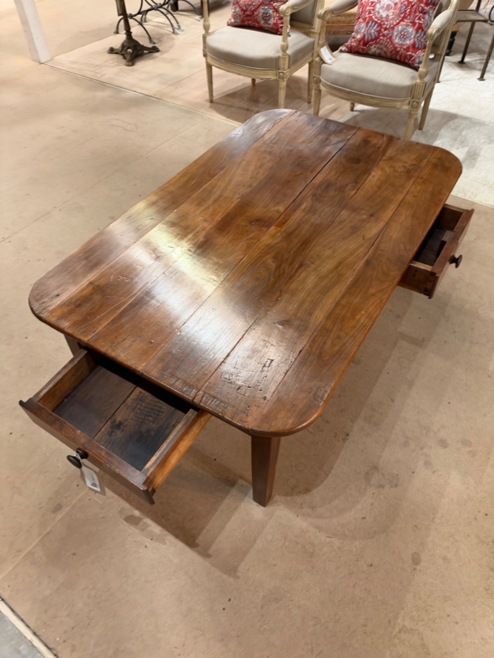 A low rectangular cherrywood coffee table featuring a plank top with rounded corners, tapered square legs, and a small side drawer. View VII