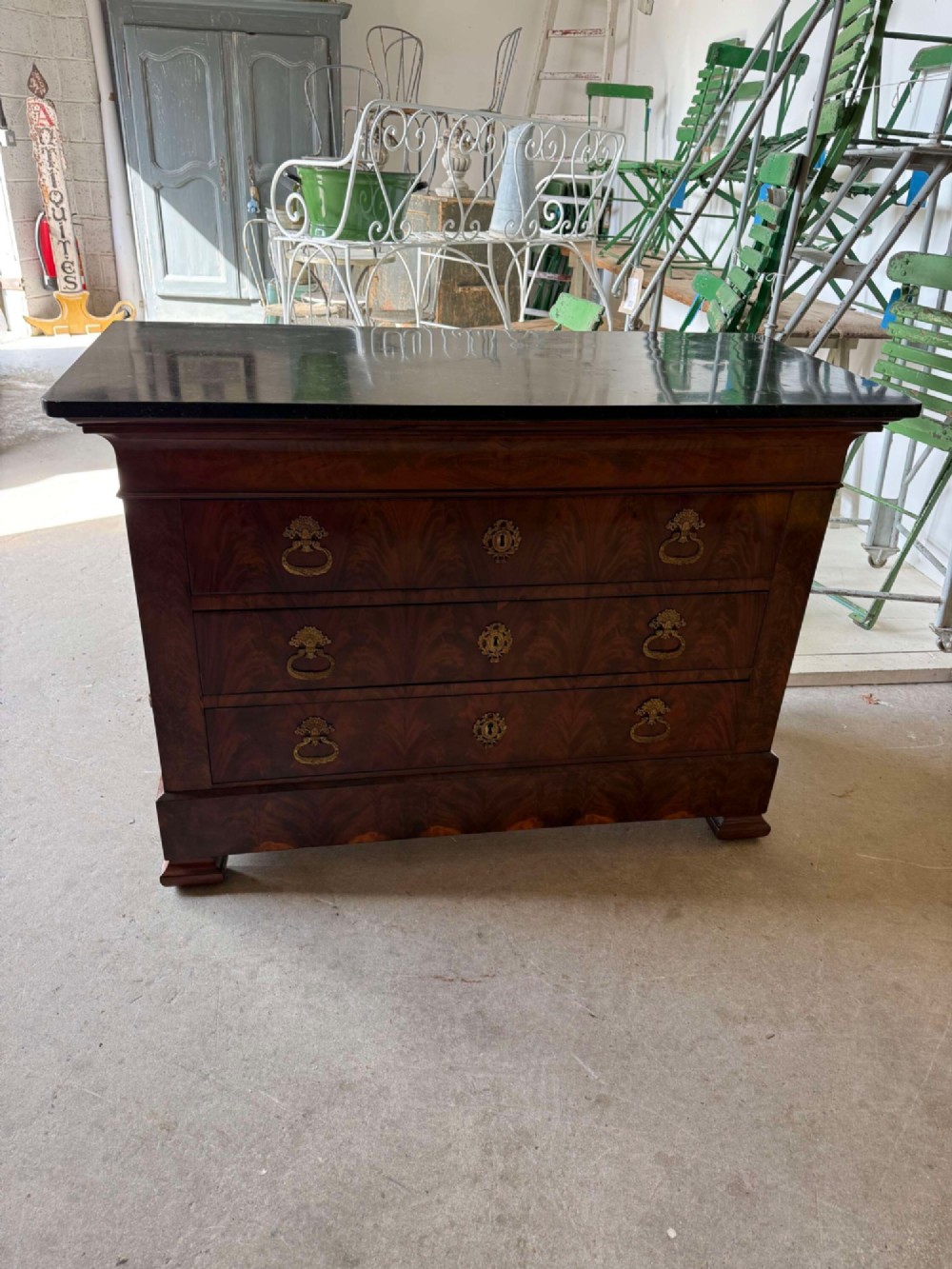 A nineteenth-century mahogany commode featuring three drawers with decorative brass handles and a dark marble top.