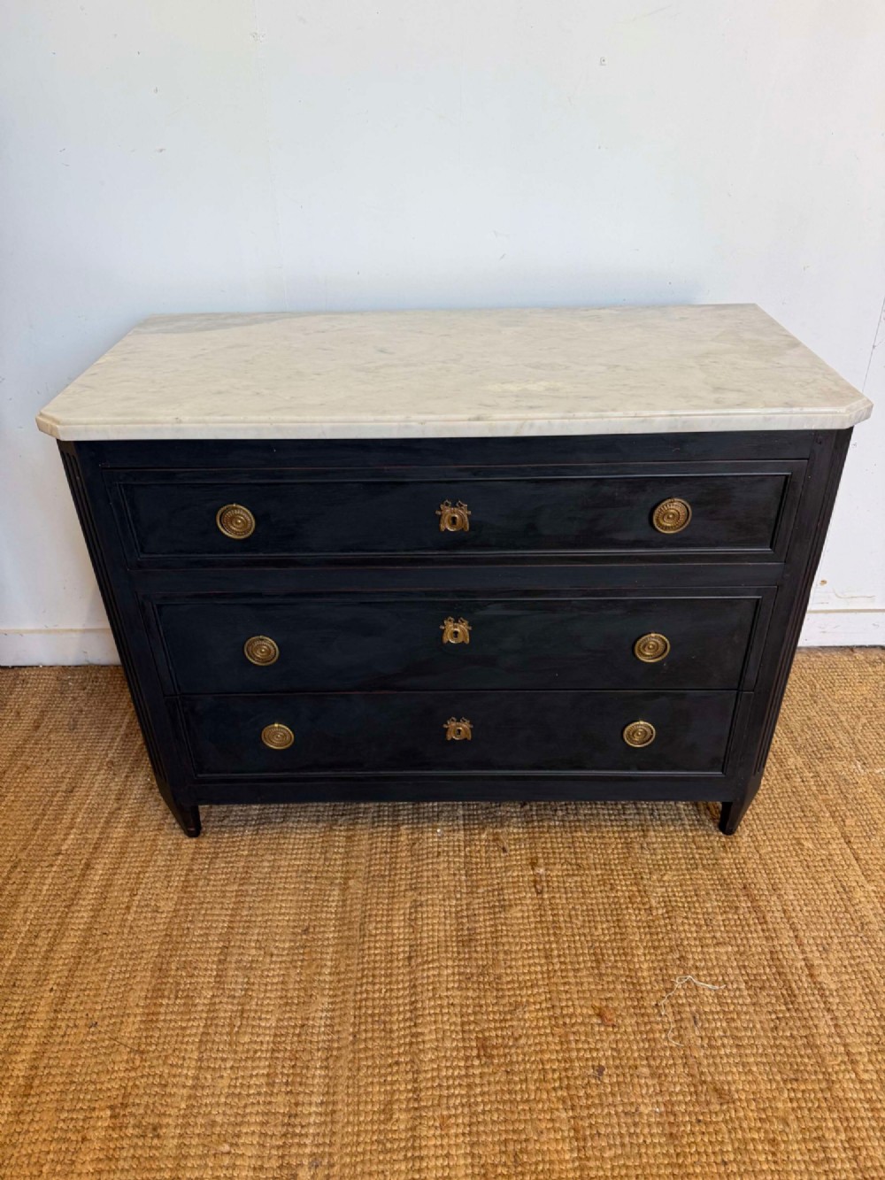 A 19th-century French three-drawer chest of drawers painted black with a white marble top and brass ring handles.