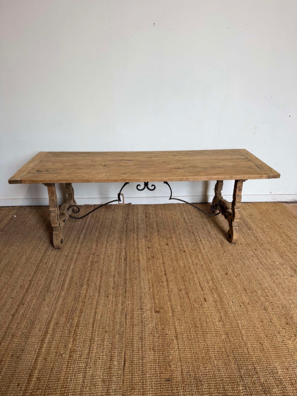 A long scrubbed oak refectory table with carved trestle legs connected by a central curved wrought iron scroll stretcher.