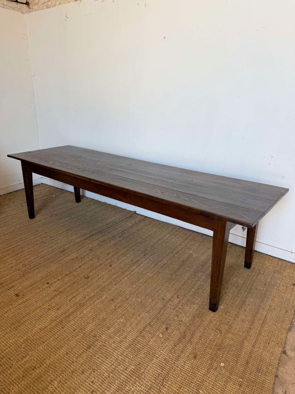 A long dark oak French farmhouse dining table featuring a plank top surface and four tapered square legs.