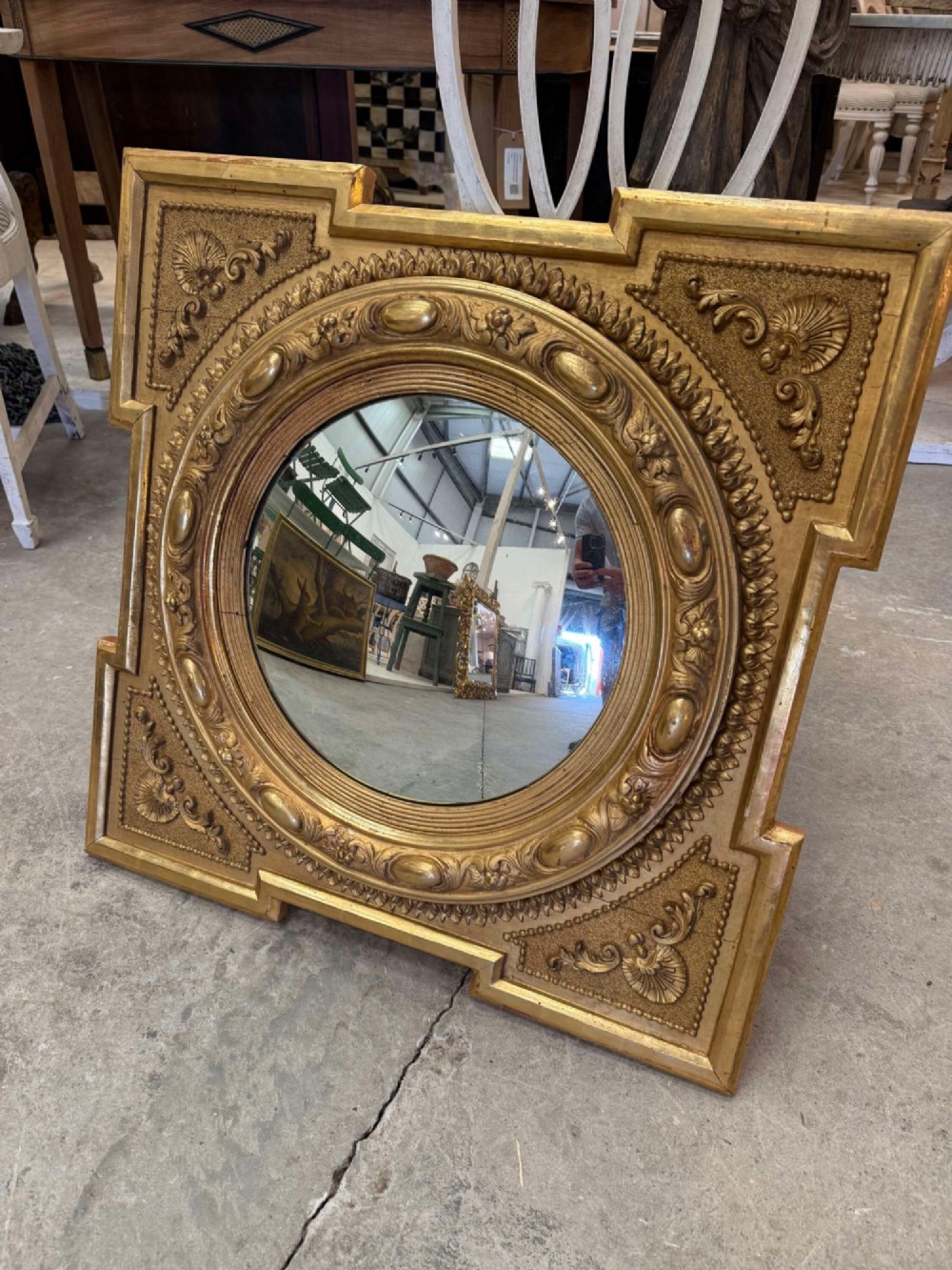 A square carved giltwood frame with detailed corner spandrels housing a central round convex glass mirror.
