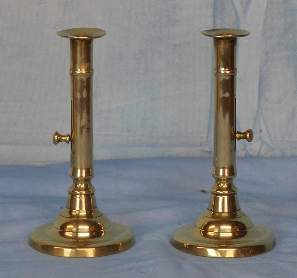 A pair of polished brass Georgian candlesticks featuring circular bases, tubular stems, and side push-up ejector mechanisms.