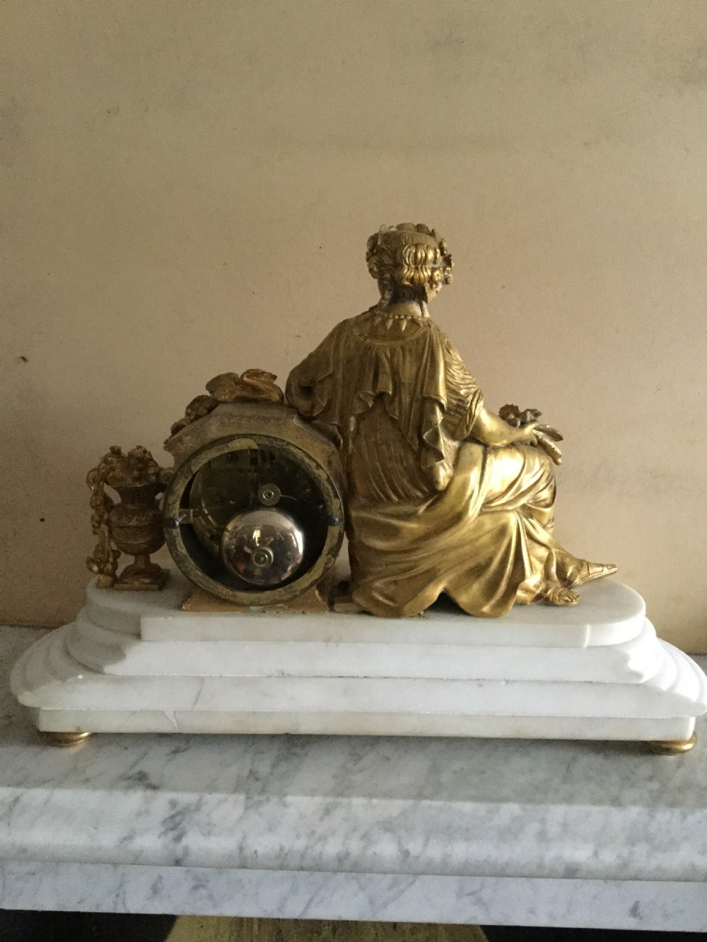 An antique French Empire mantel clock featuring a gilded bronze classical female figure leaning against a white enamel clock face set upon a stepped white marble base. View VIII