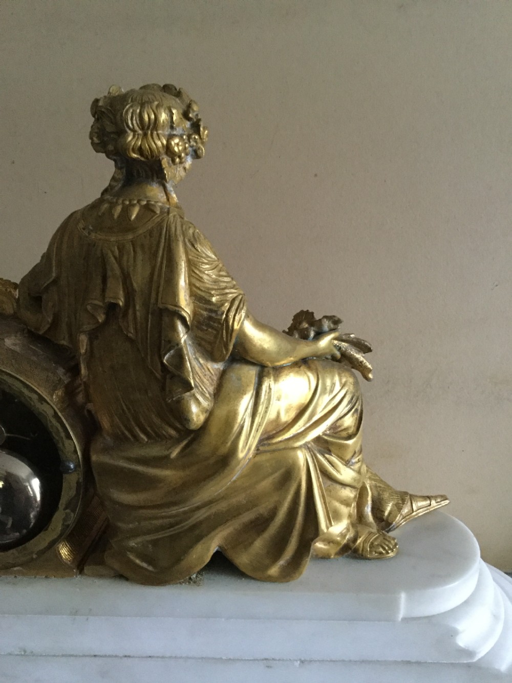 An antique French Empire mantel clock featuring a gilded bronze classical female figure leaning against a white enamel clock face set upon a stepped white marble base. View IX