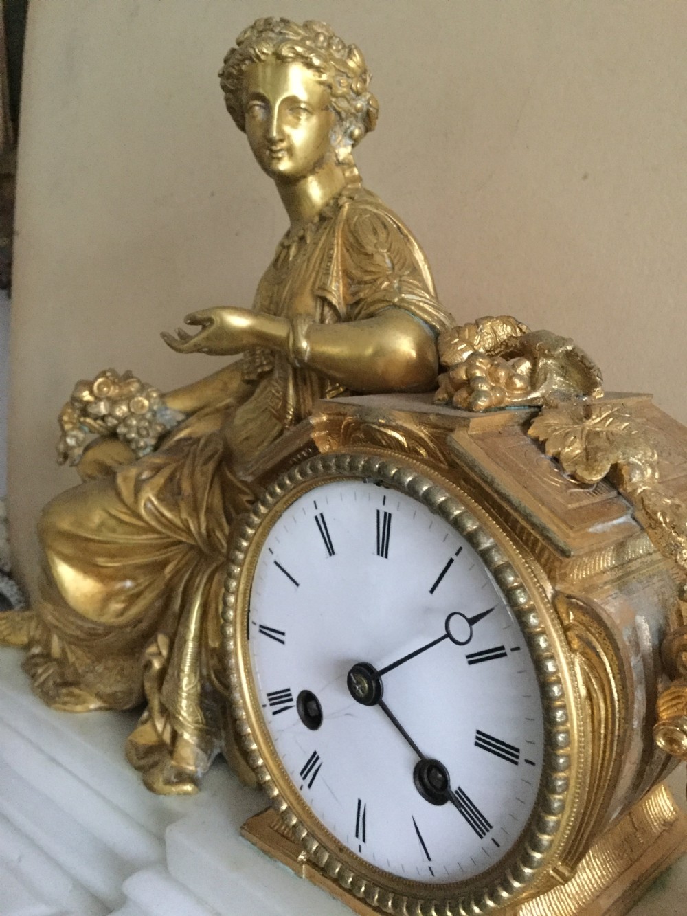 An antique French Empire mantel clock featuring a gilded bronze classical female figure leaning against a white enamel clock face set upon a stepped white marble base. View XIII