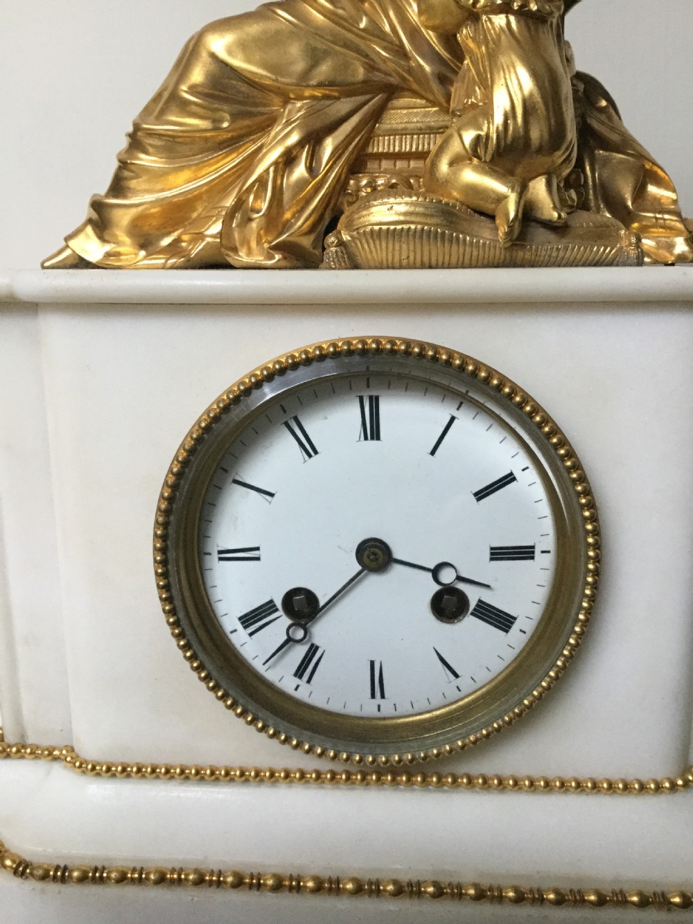 A French Neoclassical white marble mantel clock featuring a gilded bronze figural topper of a seated woman holding an open book alongside a cherub. View III