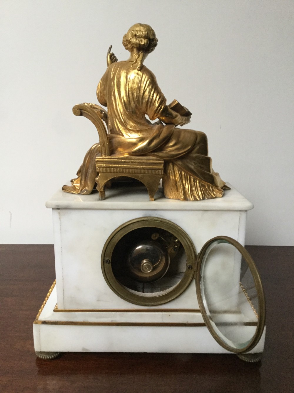 A French Neoclassical white marble mantel clock featuring a gilded bronze figural topper of a seated woman holding an open book alongside a cherub. View VII