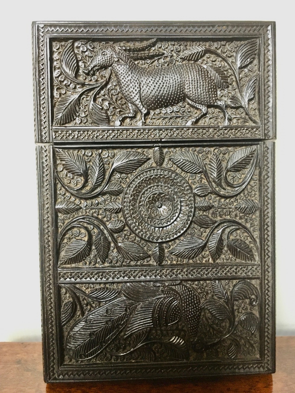 A rectangular dark carved wood card case decorated with high-relief carvings of animals, foliage, and a central circular floral motif.
