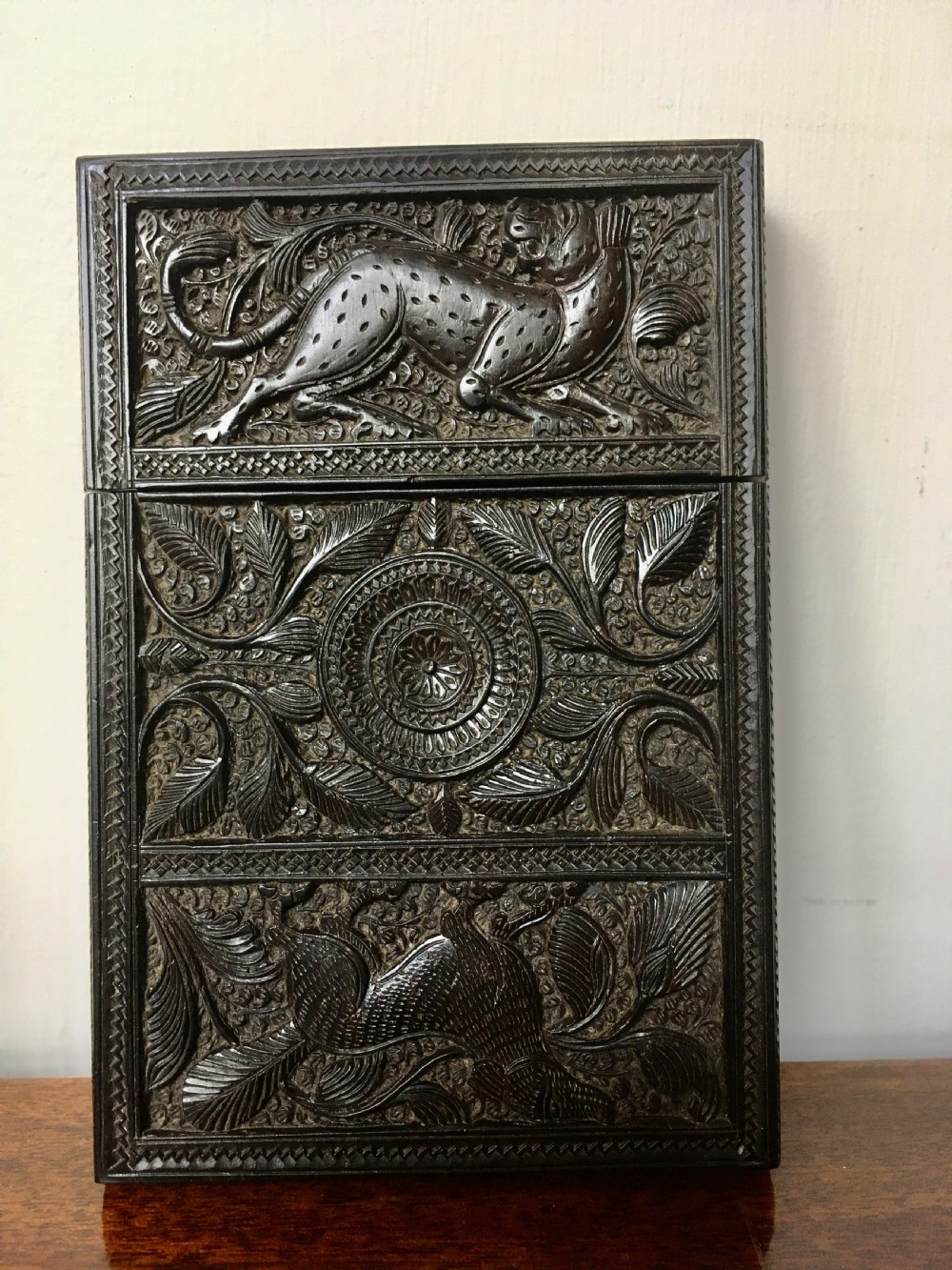 A rectangular dark carved wood card case decorated with high-relief carvings of animals, foliage, and a central circular floral motif. View II